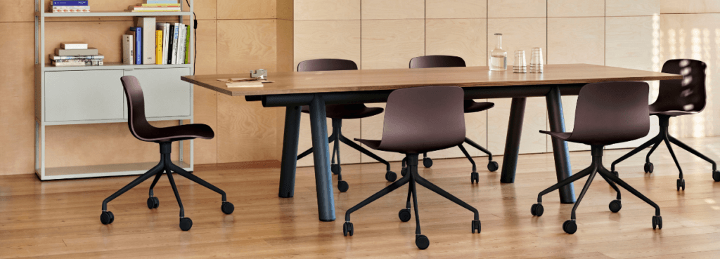 HAY AAC 14 chair in plum with black castor base around a wooden table.