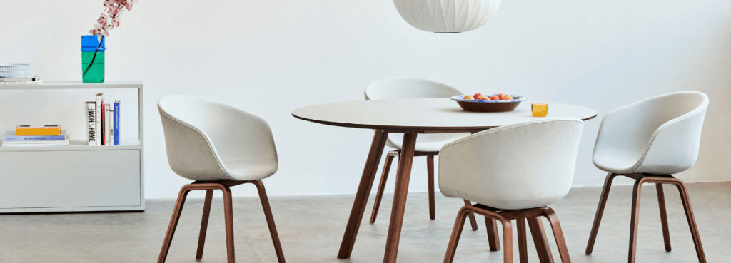 HAY AAC 23 chair. White upholstered shell with a wood base around a table. Modern design.