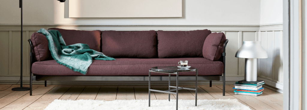 Modern plum CAN Sofa by HAY with black frame and a green throw blanket.