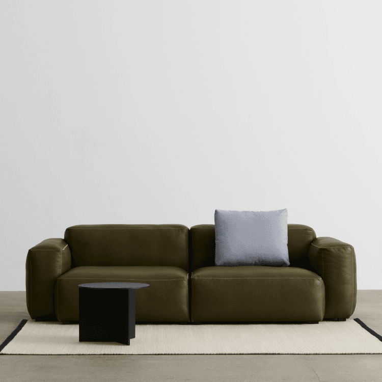 Olive green Mags Soft Low Armrest Sofa with a light blue cushion and a black side table on a white rug.