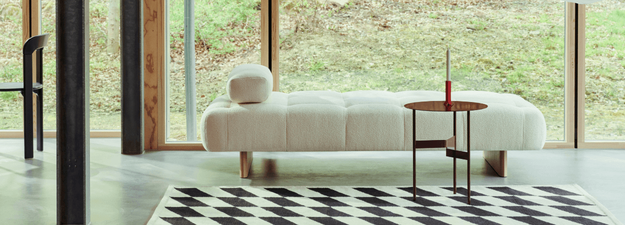 Modern cream Quilton Lift sofa with quilted texture, wooden legs, and a small round table in a bright, minimalist space.