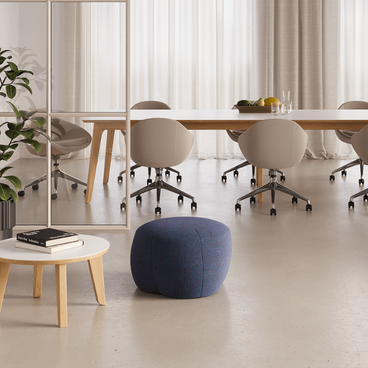 Modern office space with a blue Truffle Pouf, round, and upholstered, in front of a table with chairs.