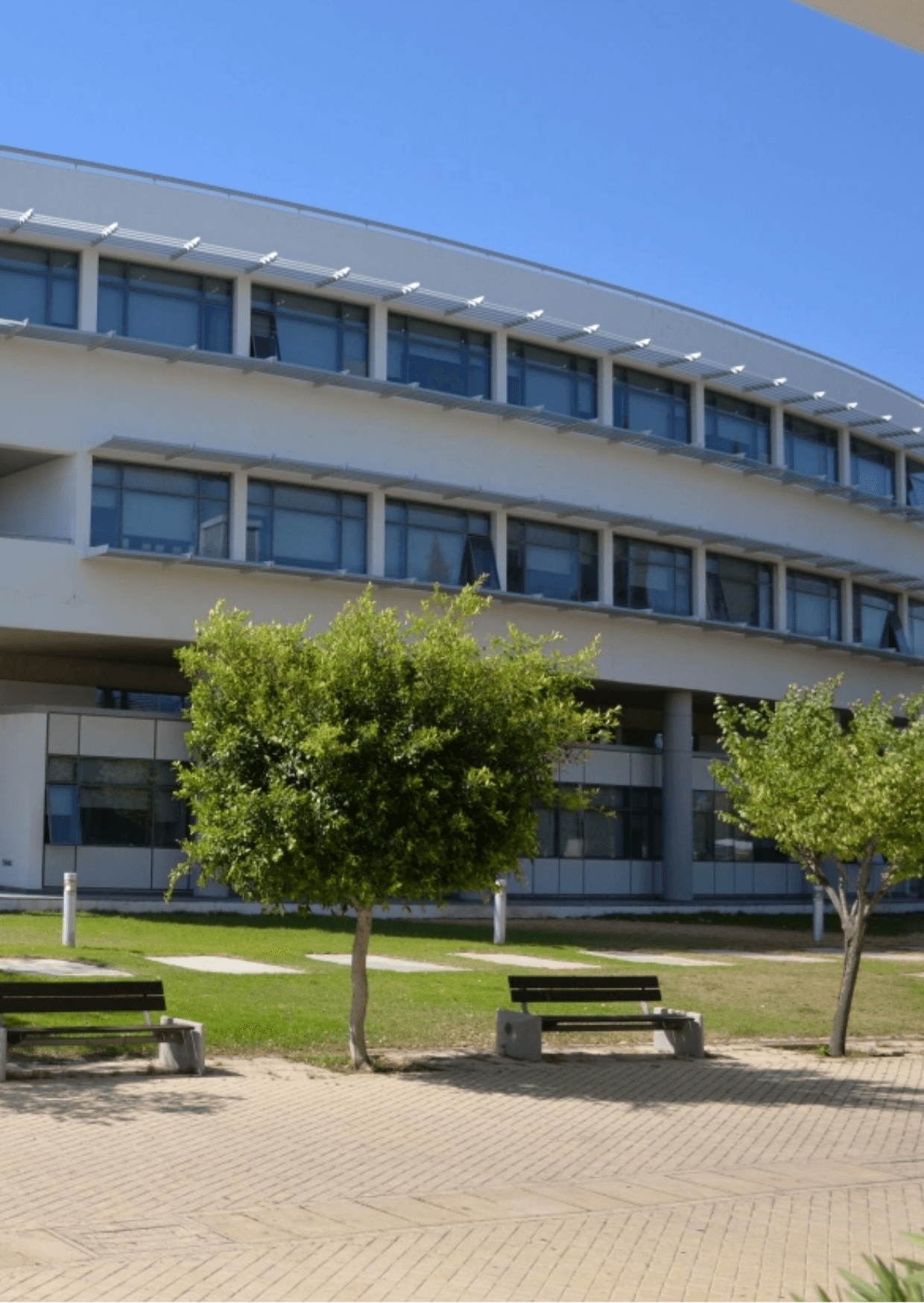 University of Cyprus Nicosia campus view. Modern building, benches, and trees under a clear blue sky.