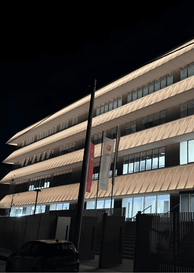 UNIC Athens Campus building at night, showcasing the illuminated facade and UNIC flags. View of UNIC.png