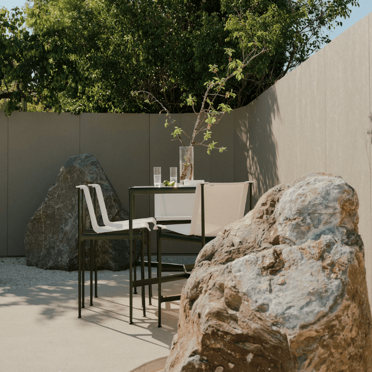 Minimalist green 1966 Stool by Knoll on a sunny terrace with a modern outdoor table and decorative rocks.