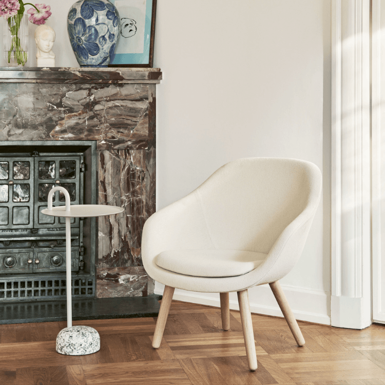 AAL 82 lounge chair in cream upholstery with solid oak legs set in a cozy living room next to a marble fireplace.