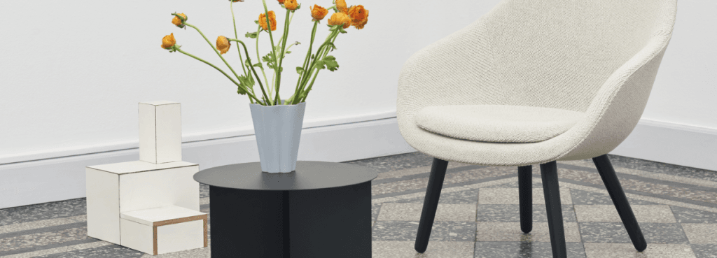 Off-white AAL 82 lounge chair with black legs beside a modern black side table and a vase of orange flowers.