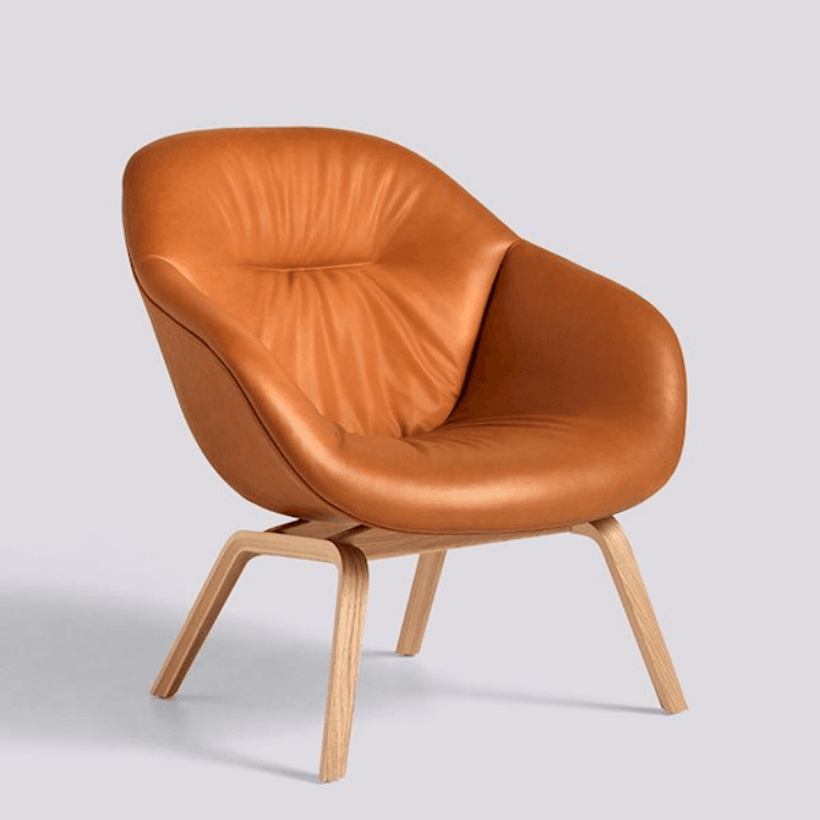AAL 83 Soft lounge chair featuring a quilted tan leather seat on a light oak plywood frame against a plain background.