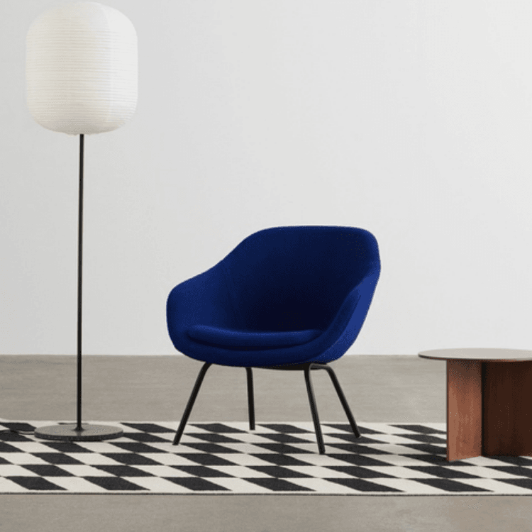 AAL 87 lounge chair in deep blue fabric with a sculpted shell design set on black steel legs against a white wall.