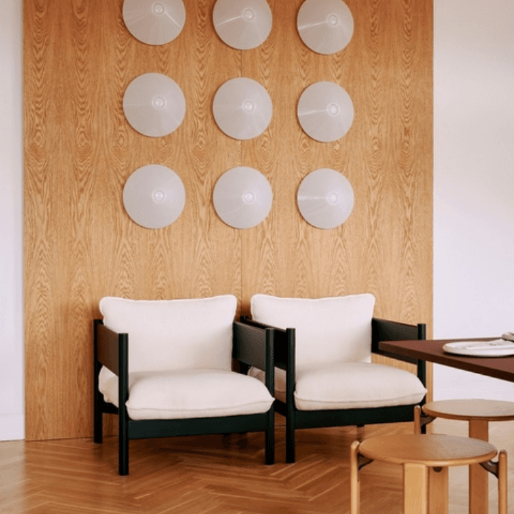 Two Arbour Club Armchairs with black frames and cream upholstery set against a wood-paneled wall with circular decor.