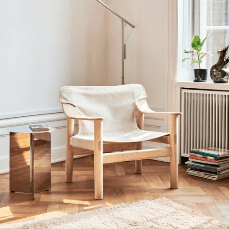 The Bernard easy chair features a light wood frame and a neutral canvas sling seat in a bright, modern living space.