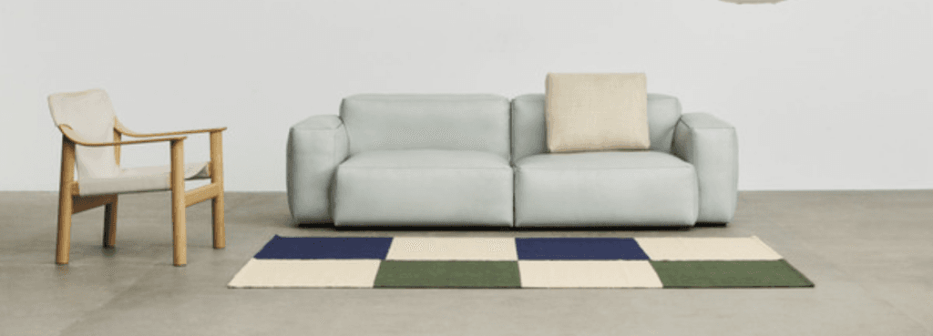 A natural wood Bernard easy chair positioned beside a modern pale blue sofa on a checkered rug.