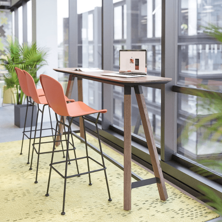 Modern Bertoia Stool with orange shell seat and black wire frame at a slim wood bar table in a bright office space.