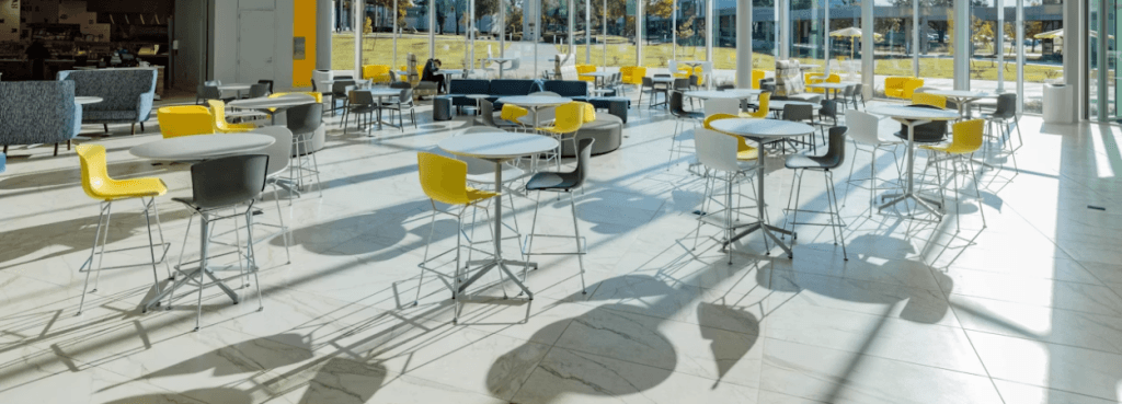 Bertoia Stool collection featuring yellow and grey contoured shell seats arranged around high tables in a sunny atrium.