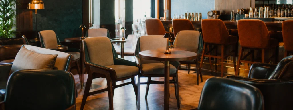 Modern café furniture featuring upholstered chairs and wooden tables with small lamps in a warm, ambient indoor setting.