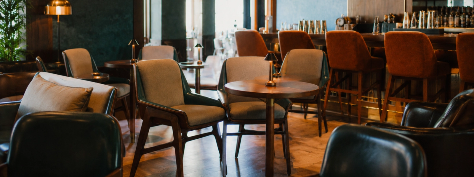 Modern café furniture featuring upholstered chairs and wooden tables with small lamps in a warm, ambient indoor setting.