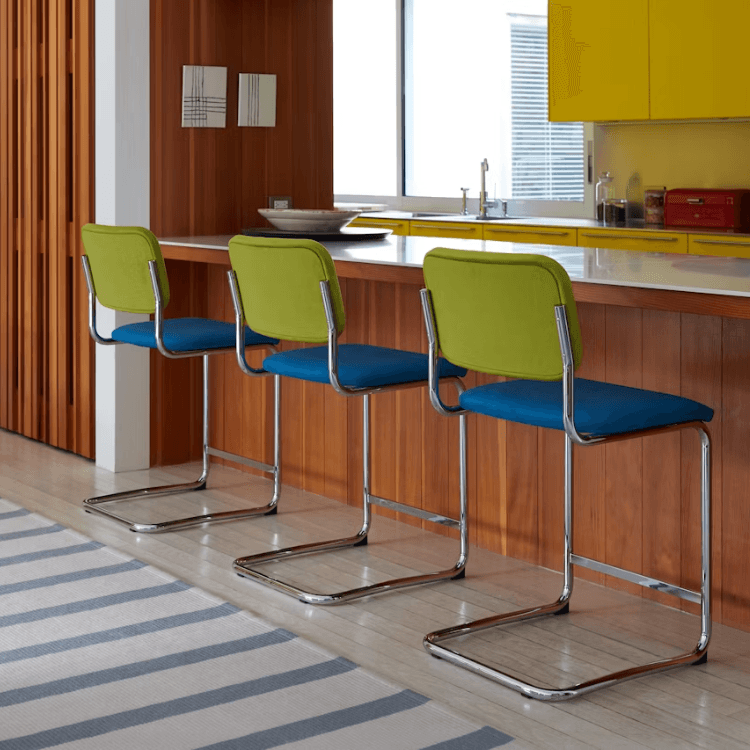 Three Cesca Stools with tubular steel frames, bright blue seats, and lime green backrests at a wooden kitchen island.