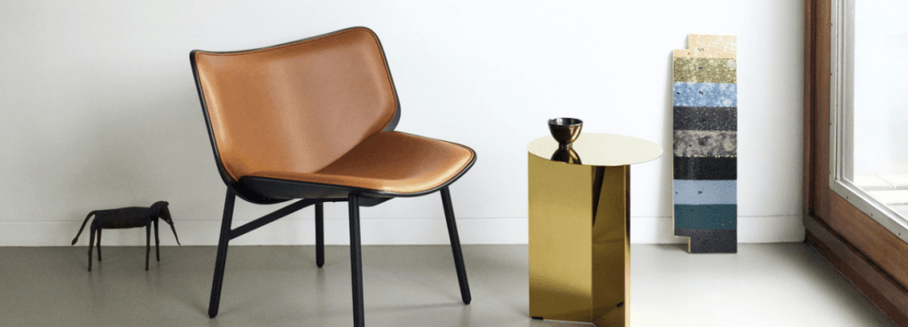 Dapper lounge chair featuring cognac leather upholstery on a black frame next to a sleek metallic gold side table.