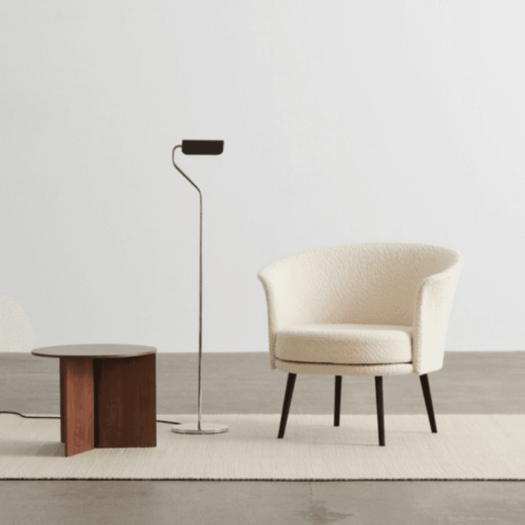 Dorso swivel lounge chair in cream textured fabric with black legs, placed beside a wooden side table and floor lamp.