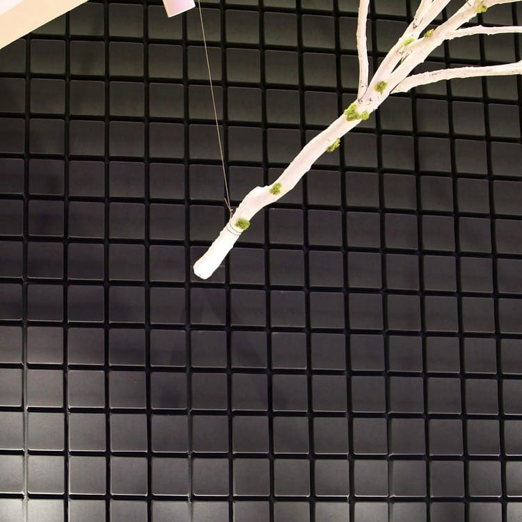 Deeply textured Key Grid acoustic wall featuring dark, raised squares and a decorative white twig branch.