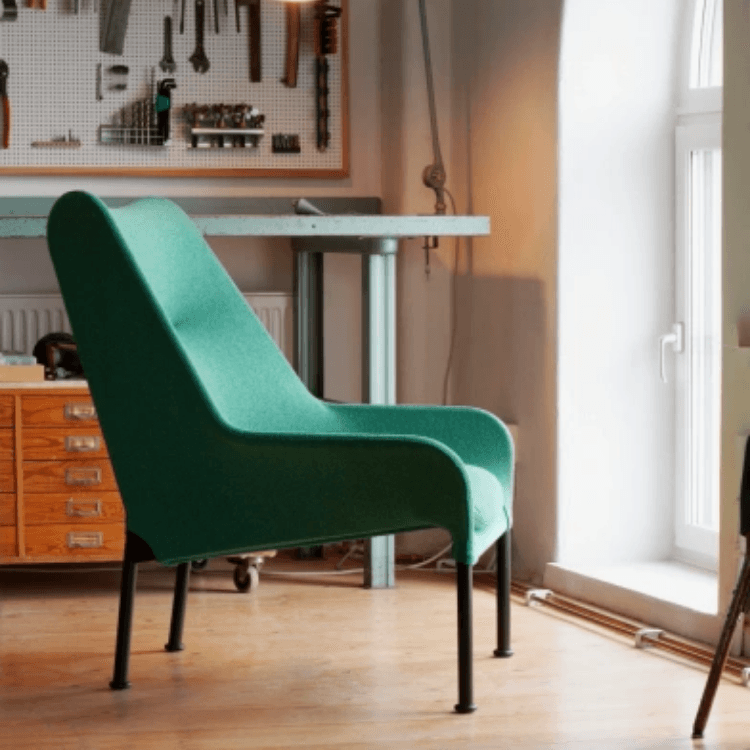 Minimalist green O2 Lounge Chair with sleek fabric upholstery and black legs in a bright workshop setting.