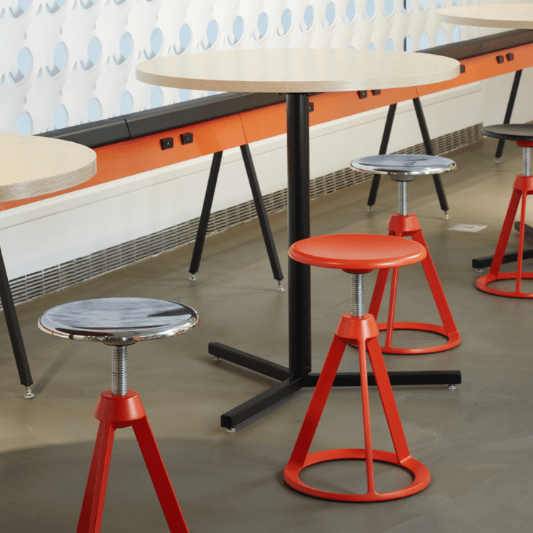 Piton Stool featuring a bright orange tripod base and adjustable metal seat in a contemporary shared workspace.