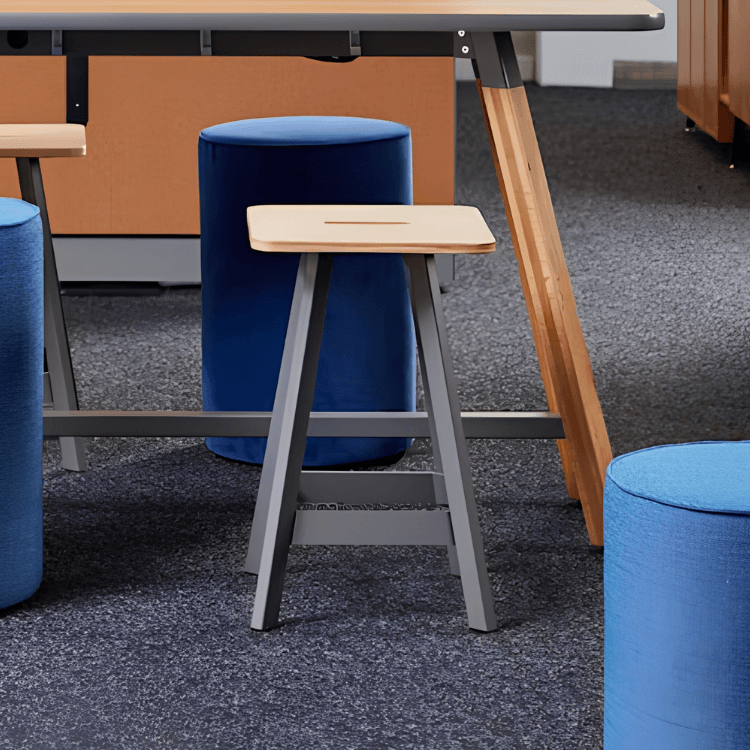 Rockwell Unscripted Easy Stools with light wood seats and grey frames positioned near blue fabric stools in a workspace.