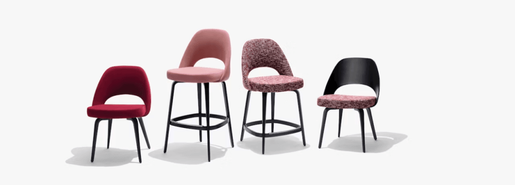 Four Saarinen Executive Stools with varying heights and diverse pink, red, and patterned textile upholstery.
