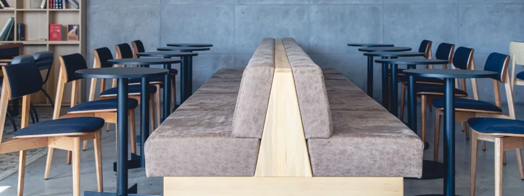 Modern school cafeteria furniture featuring a central back-to-back bench with wooden base and circular black bistro tables.