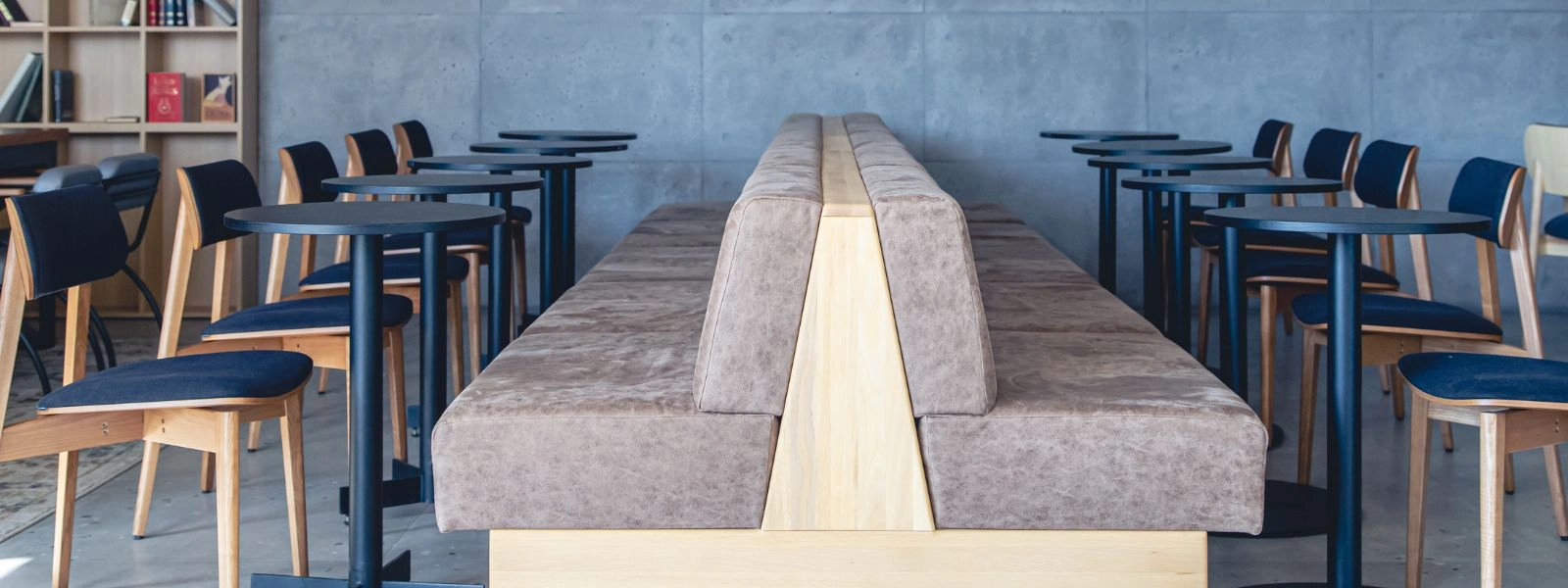Modern school cafeteria furniture featuring a central back-to-back bench with wooden base and circular black bistro tables.
