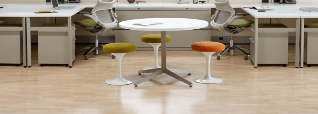 Three colorful Knoll Tulip Stools with fabric cushions arranged around a central white table in a bright workspace.