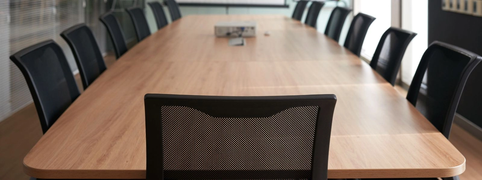 Large wooden conference table surrounded by black mesh chairs in a modern office meeting room setting.