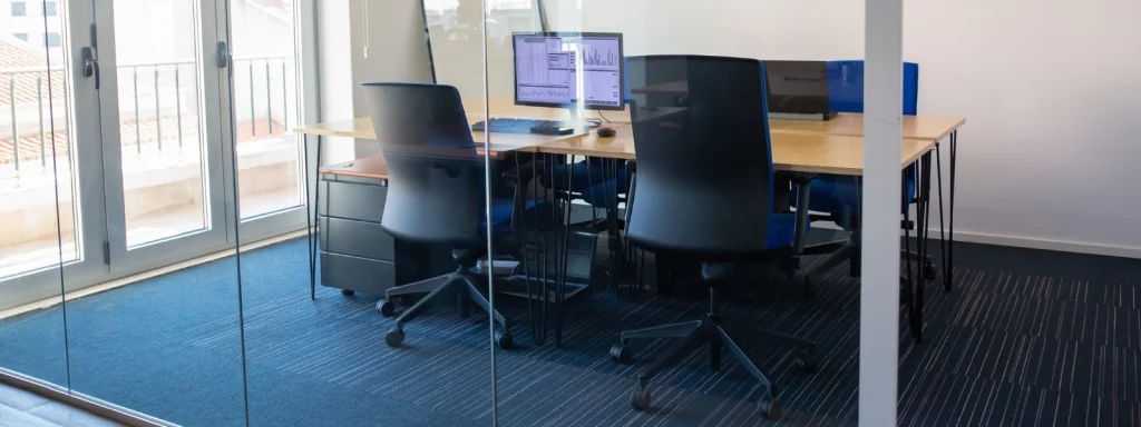 Modern soundproof pod with desks, black ergonomic chairs, and computer monitors inside a glass-walled office space.