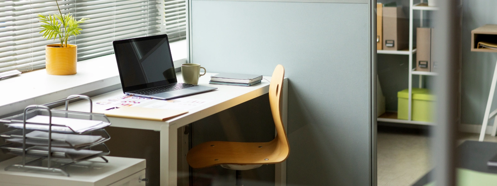 Modern office workstation setup with a laptop, wooden chair, and desk accessories for a hybrid workplace environment.